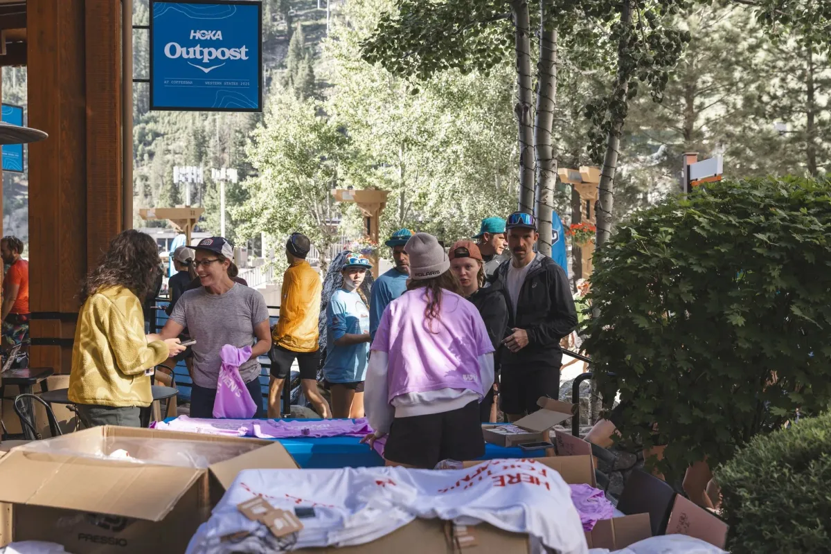 A brand activation tent at a trail race, tables stacked with Here for the Women's Race shirts, runners queueing.